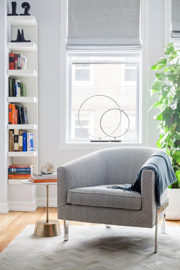 A cozy reading nook by the window features an upholstered chair, a small side table and an IKEA bookshelf in the corner