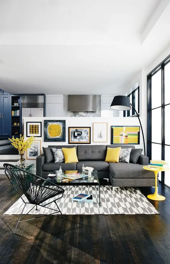 modern living room with a grey sofa, yellow pillows, a table, an artwork and dark floors
