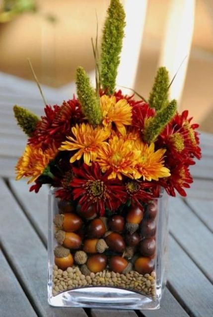 acorns put into a glass vase and a bold floral arrangement over them