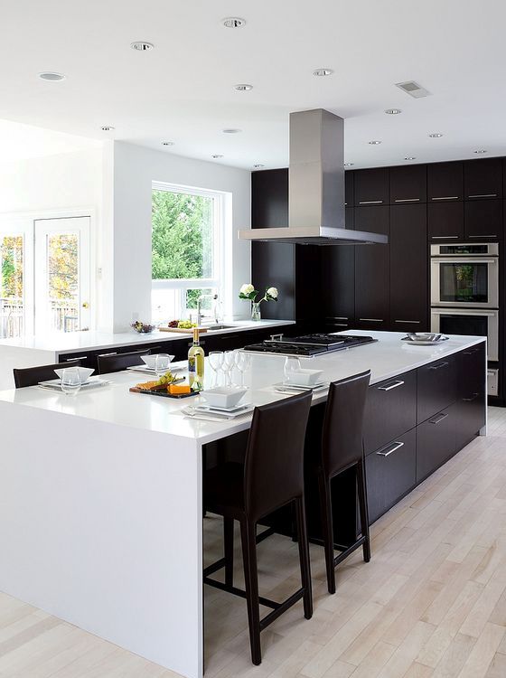 Modern black and white kitchen with light colored wooden floors and a steel hood