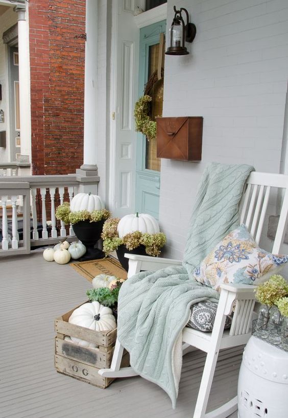 white pumpkins, a white rocker and a pastel blanket and pillow