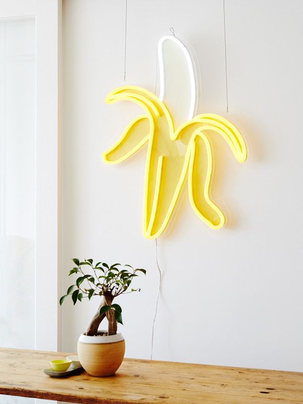A banana neon light would shine on a neutral gray wall.