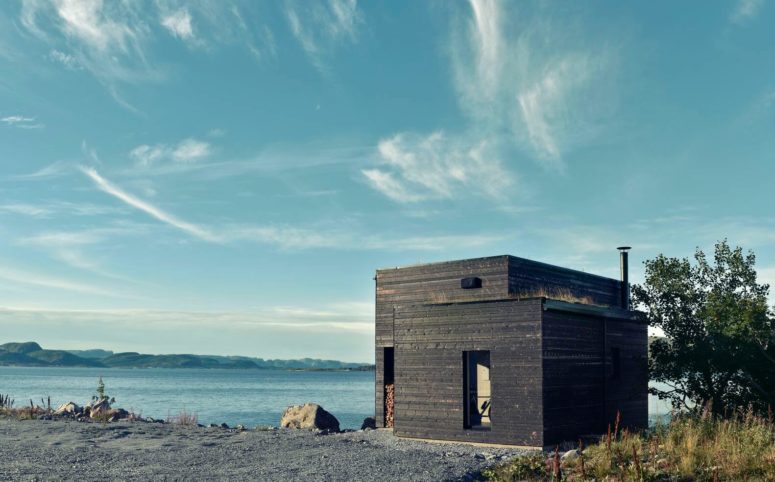 This dark wooden cabin is located on a northern coast, and it features Scandinavian design with some coastal touches
