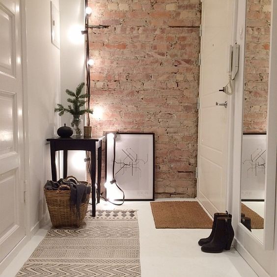 small decluttered entryway with an exposed brick wall, lights and a tall mirror