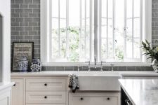 a white farmhouse kitchen with grey subway tiles all over the kitchen wall and white stone countertops is a chic space