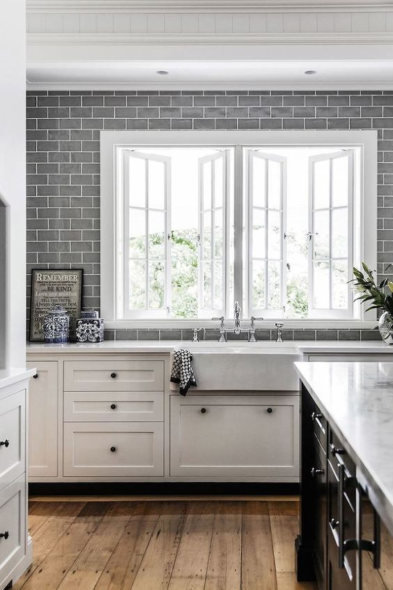 a white farmhouse kitchen with grey subway tiles all over the kitchen wall and white stone countertops is a chic space