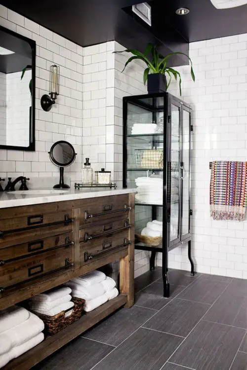 a rustic meets industrial bathroom with white subway tiles on the walls and large scale tiles on the floor, with black touches and fixtures