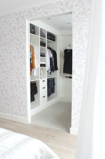 Very small walk in closet in white with a leading rack on the left wall