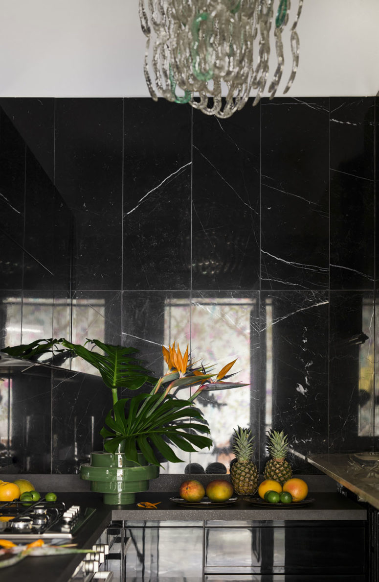 The kitchen is a sleek all-black one, with black marble walls and black stone countetops