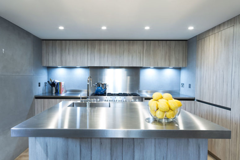 The kitchen is decorated in light grey, concrete and stainless steel, there are a lot of lights