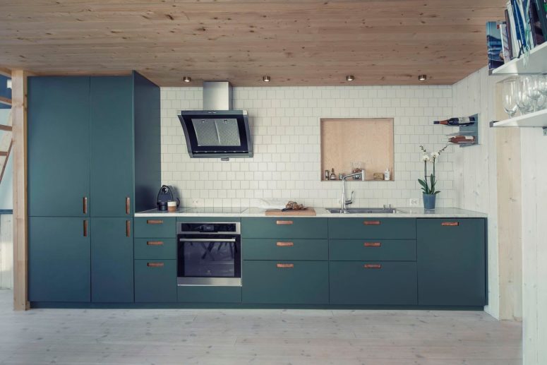 The kitchen has modern blue cabinets and drawers, a cool warm wooden ceiling and a whitewashed floor