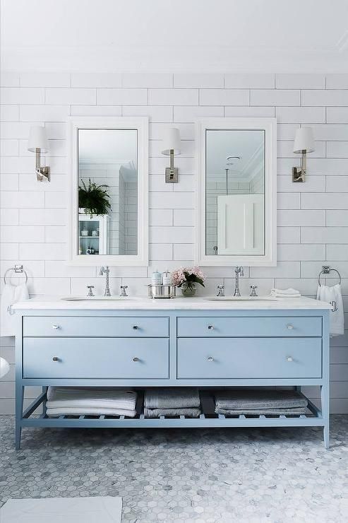 a serene and airy bathroom with subway tiles on the walls, marble hex tiles on the floor, a pale blue vanity and a couple of mirrors and lamps