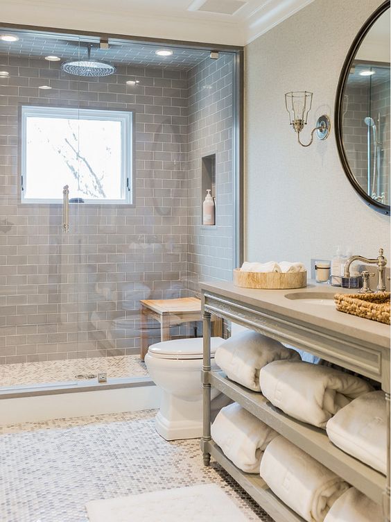 a modern neutral bathroom with grey subway tiles highlighting the shower space and penny tiles on the floor plus a vintage vanity