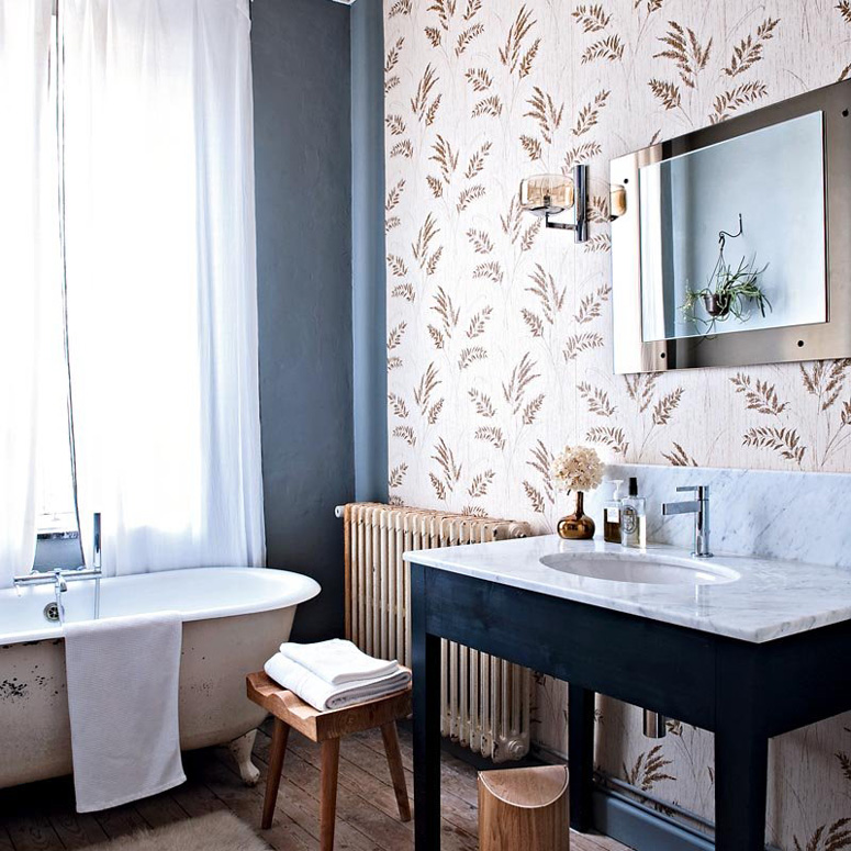 The master bathroom has a rural print wallpaper wall, a modern mirror and faucet and lots of rustic touches