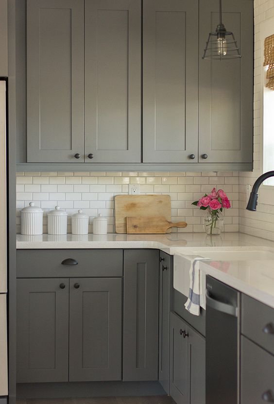 a stylish grey farmhouse kitchen with a white subway tile backsplash and white countertops plus black fixtures and pendant lamps