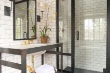 a vintage bathroom clad with white subway tiles, dark large scale ones on the floor, black frames and fixtures and greenery