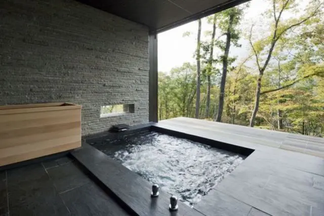 black tiles and the use of stone in this indoor-outdoor bathing space give it a minimal Japanese look