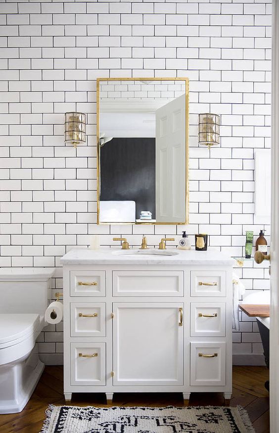 An elegant white bathroom with white subway tiles, a black free standing bathtub, gold touches and fixtures for more glam