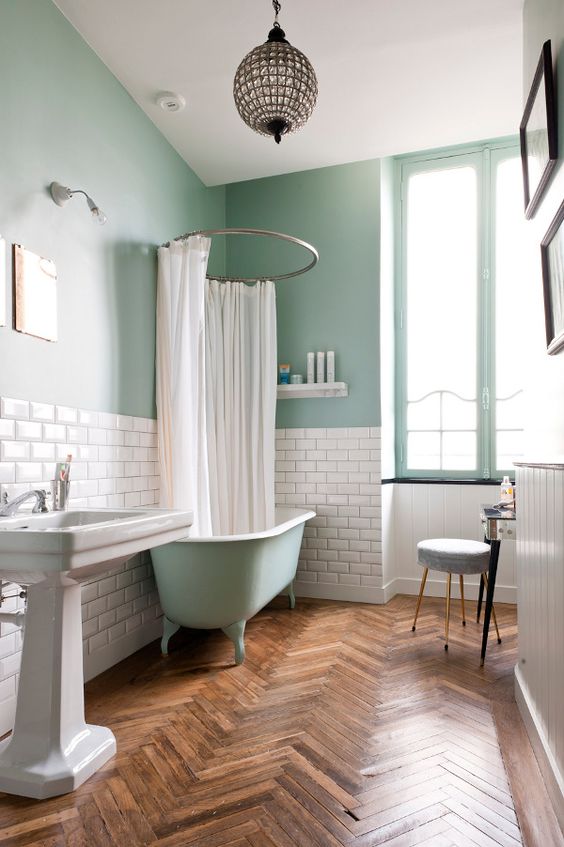 A dreamy aqua colored bathroom with subway tiles used for a backsplash, a free standing sink and a sphere pendant lamp