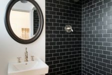 a bold bathroom with black subway tiles in the shower, black hex tiles on the floor, a mirror in a black frame and wall-mounted  sink