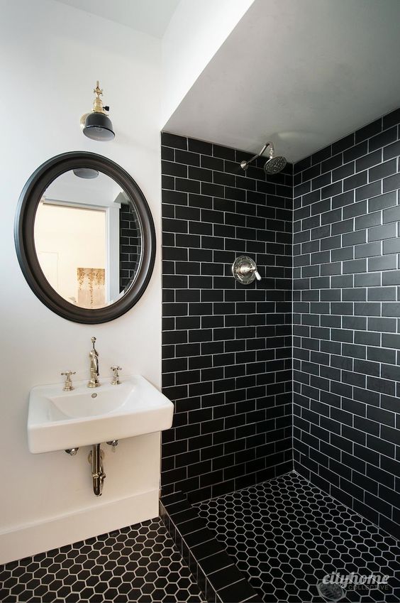A bold bathroom with black subway tiles in the shower, black hex tiles on the floor, a mirror in a black frame and wall mounted  sink