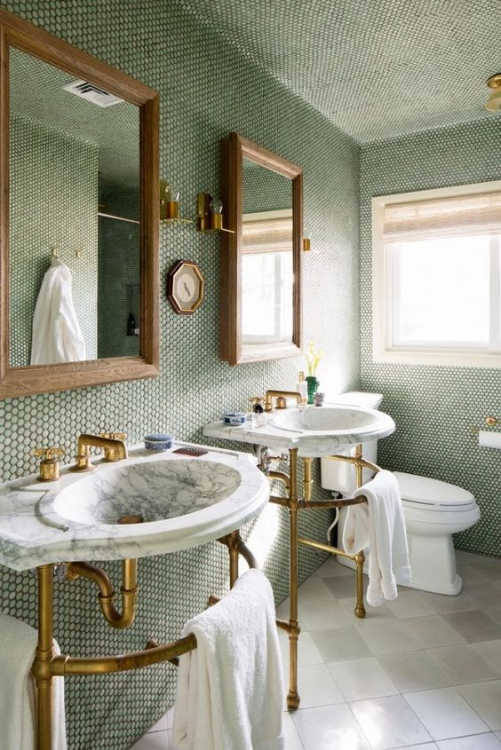 bathroom with brass and marble fixtures and a wall of moss-green penny tiles