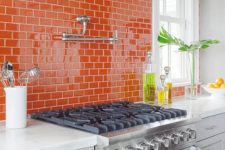 a white farmhouse kitchen with a bold orange subway tile backsplash and white countertops is a cool and vibrant space