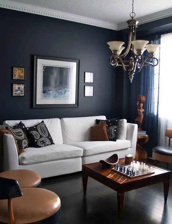 masculine space with a dark navy accent wall, tan chairs, warm wood furniture and accessories