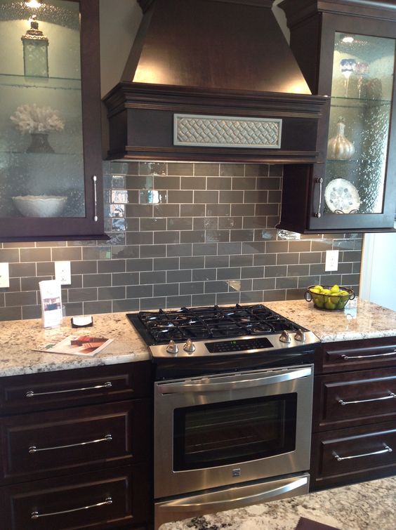 gray glass subway tile backsplash with dark brown cabinets and stainless steel appliances