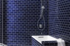 a laconic bathroom clad with navy blue subway tiles completely, with white details and a white chair for an ultimately bold look