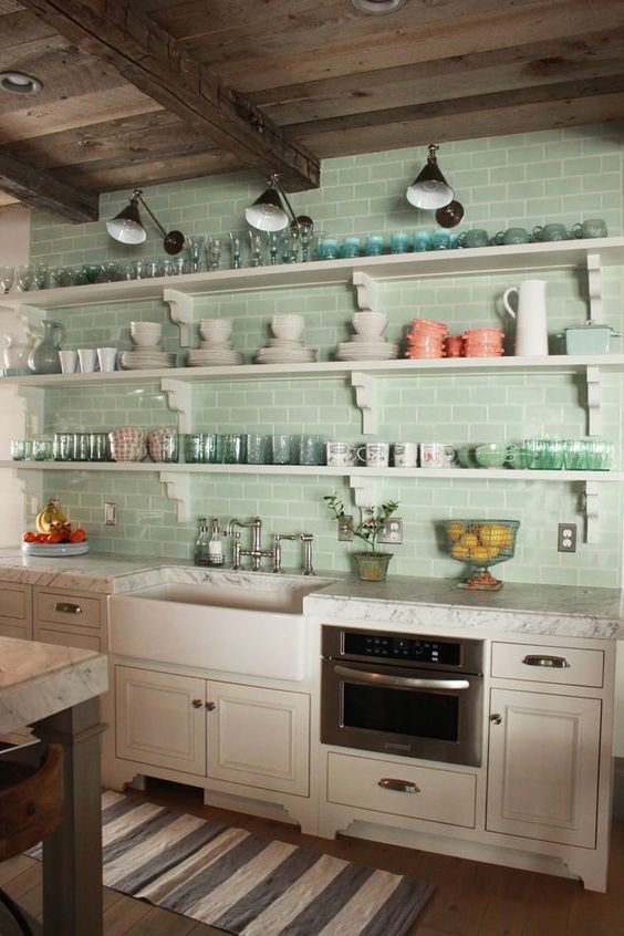 Aqua colored subway tiles covering the whole wall infuse the kitchen with color and substitute upper cabinets