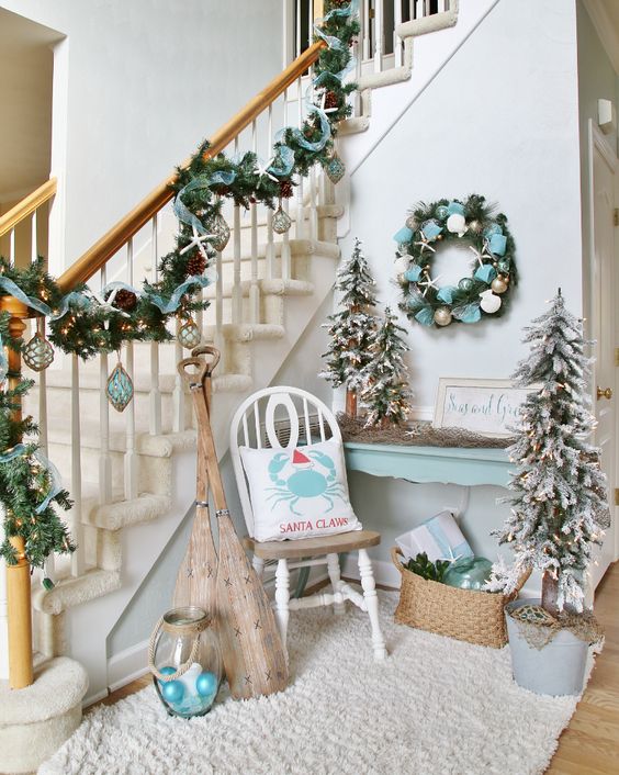 coastal Christmas entryway decor in pale blue, with a garland, a wreath, some trees and ornaments