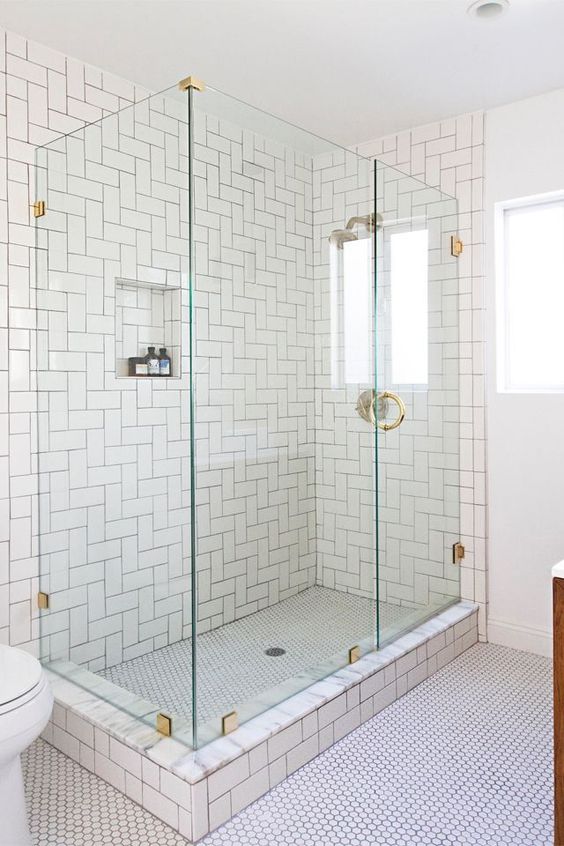 white subway tiles in the shower clad in a creative herringbone pattern create a bold space without adding color and look cohesive with penny tiles on the floor