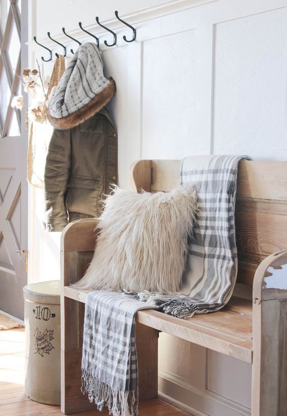 Simple farmhouse entryway is perfectly decorated for winter with large coat hooks, a rustic bench, and a place for snow covered boots