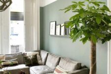 a Nordic living room with a green accent wall, a low grey sofa, a couple of coffee tables, a ledge gallery wall and a potted tree