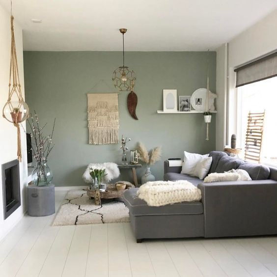 A boho living room with a green accent wall, a grey sectional, a built in fireplace, a lot of cool and catchy boho home decor