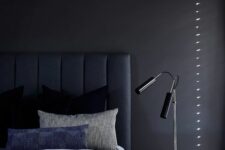 a chic and peaceful moody bedroom with a black accent wall, a navy upholstered bed and blue bedding, a nightstand, black table lamps
