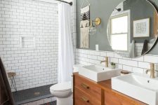 a chic mid-century modern bathroom with a grey accent wall penny and subway tiles, a stained vanity, a round mirror and two sinks