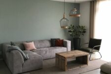 a cozy living room with a green accent wall, a low grey sofa, a stained coffee table, a dark green chair and a couple of pendant lamps