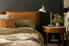 a cozy moody bedroom with soot walls, a bed with amber leather upholstery, neutral bedding, a chic nightstand and a printed rug