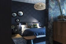 a dark and moody bedroom with navy walls and a white ceiling, black modern furniture, a printed statement wall and an arrangement of mirrors