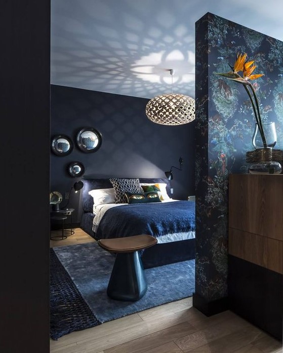 a dark and moody bedroom with navy walls and a white ceiling, black modern furniture, a printed statement wall and an arrangement of mirrors