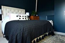 a dark bedroom with navy walls, some niches, an upholstered bed with contrasting bedding, a printed rug and a cool chandelier