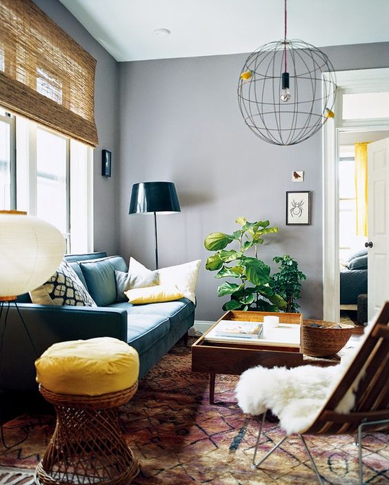 A mid century modern living room with grey walls, a green sofa, some stained furniture, a bold stool, a sphere pendant lamp and a potted plant