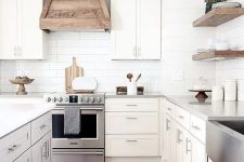 a modern country kitchen with shaker style cabinets, a white subway tile backsplash, a wooden hood and floating shelves