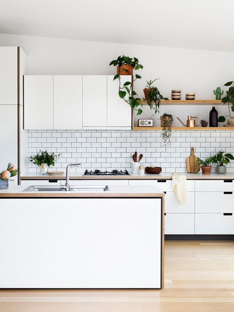a modern white kitchen with butcherblock countertops, a white subway tile backsplash, a kitchen island and potted plants