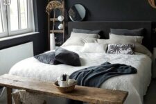 a moody bedroom with black walls, a grey upholstered bed, neutral bedding, a rough stained bench, baskets and a ladder plus some wabi-sabi decor