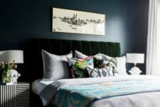 a moody bedroom with navy walls and a ceiling, a dark green velvet bed, a glam gold chandelier and striped nightstands