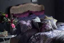 a moody vintage bedroom with black walls, a rattan bed, a gallery wall, a little nightstand and a pendant lamp