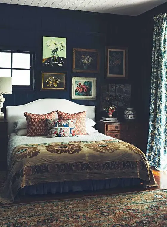 a moody vintage bedroom with dark walls but a light ceiling, a cofy bed and vintage furniture, a gallery wall and printed textiles